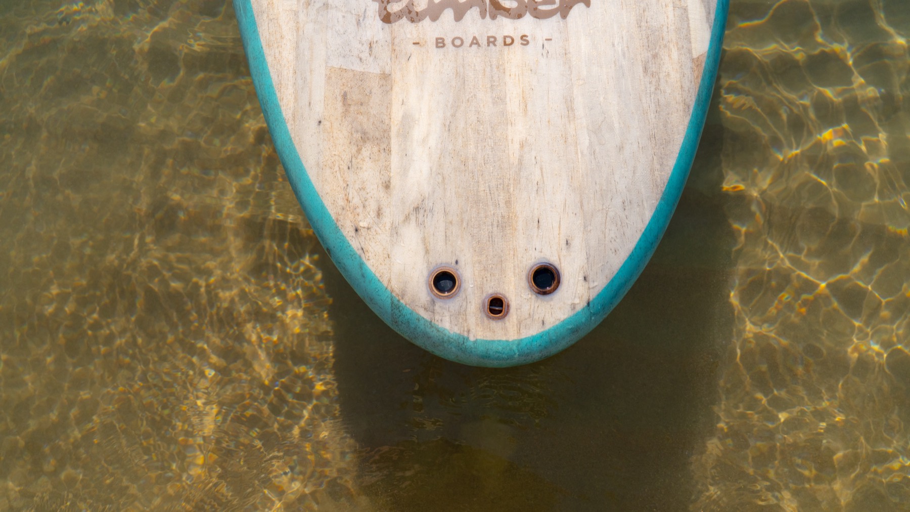 The nose of the Agave 10 with its teal rail, resting in clear shallow water